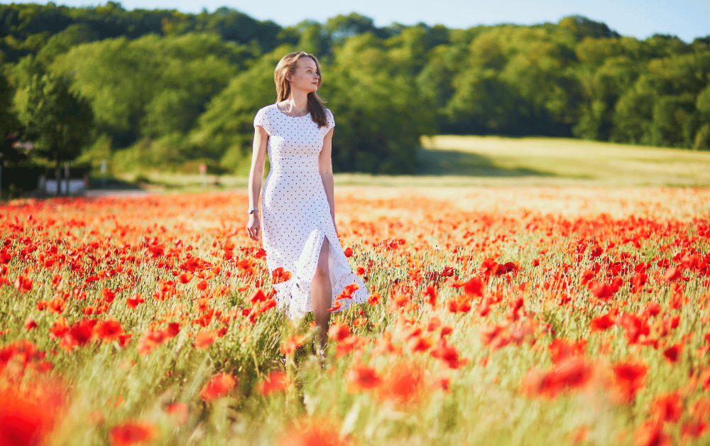 A woman in a flowing dress walks peacefully through a vibrant poppy field, symbolizing the benefits of walking for self-care, relaxation, and mental well-being.