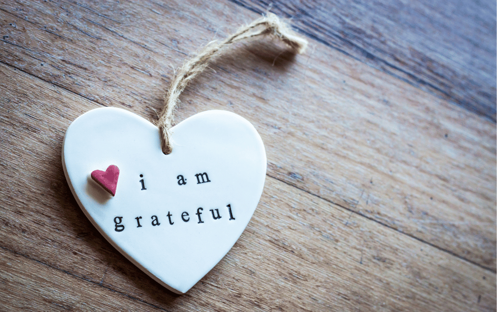 A small tag with the words "I am grateful." written on it, resting on a rustic wooden table. The scene evokes a sense of reflection and appreciation, symbolizing things to be grateful for.