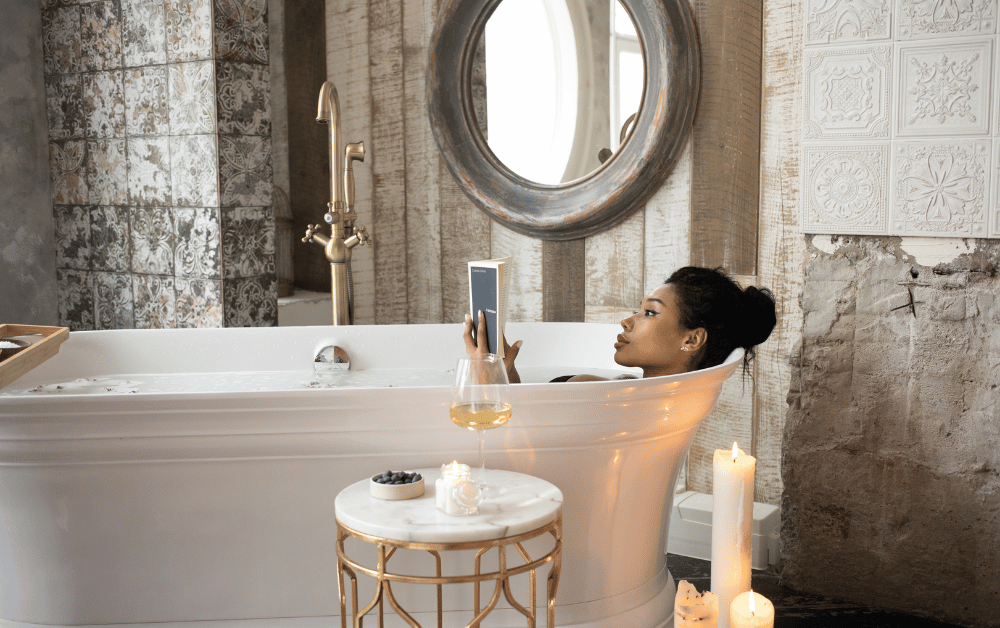 A woman relaxing in a warm bath while reading a book, surrounded by soft lighting and a peaceful atmosphere—illustrating how a bath can improve mental health and promote relaxation.