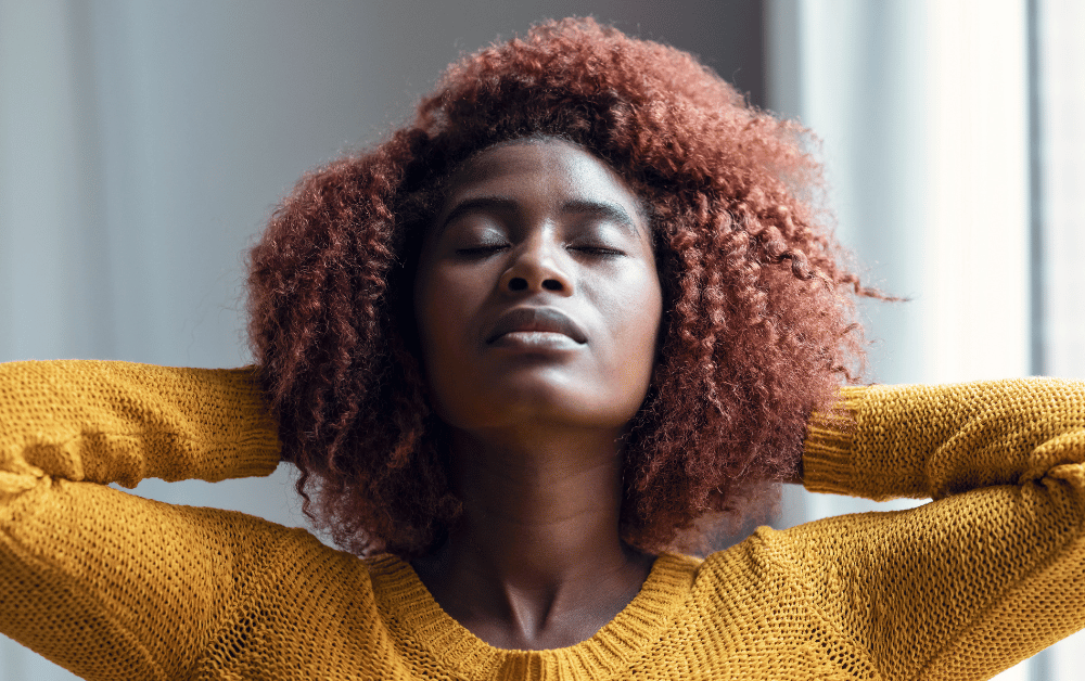 A woman stretching her arms upward and taking a deep breath in a calm setting, demonstrating deep breathing for stress relief and relaxation.