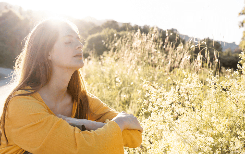 Woman sitting outside in the sun, enjoying the benefits of sunlight for mental health, relaxation, and emotional well-being.