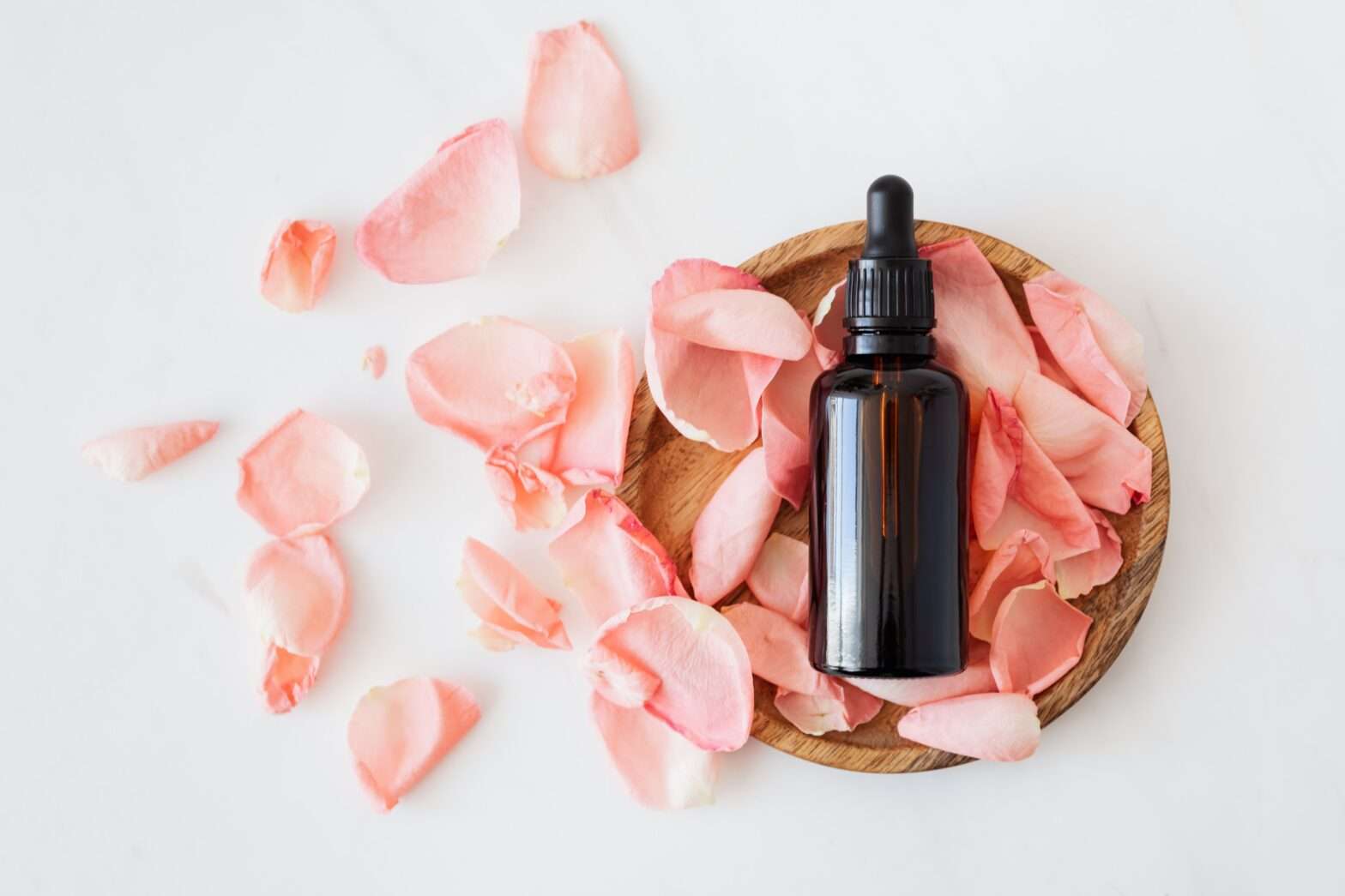 Glass essential oil bottle with pink flower petals around it, representing essential oil diffuser benefits for mental health and relaxation.