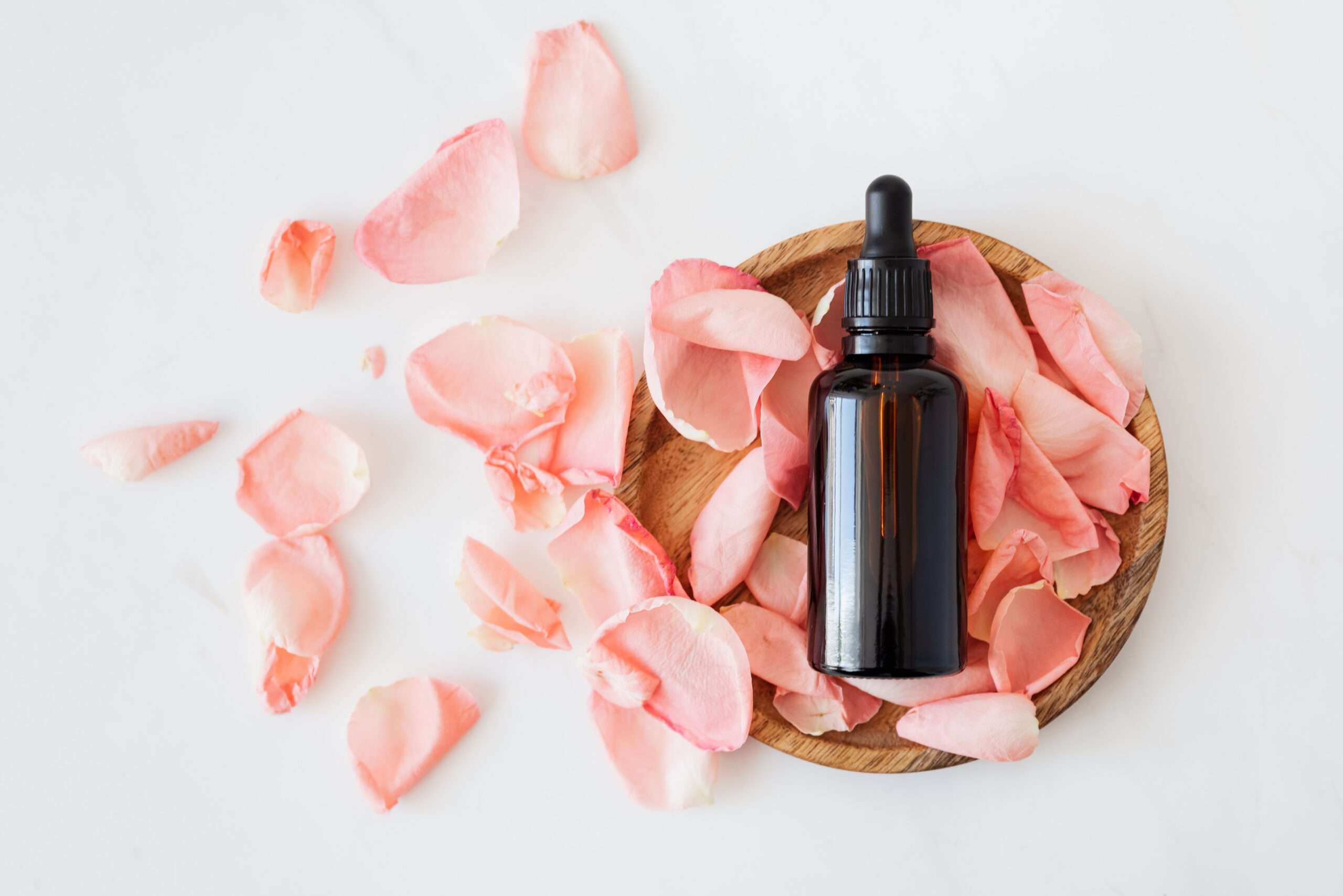 Glass essential oil bottle with pink flower petals around it, representing essential oil diffuser blends benefits for mental health and relaxation.