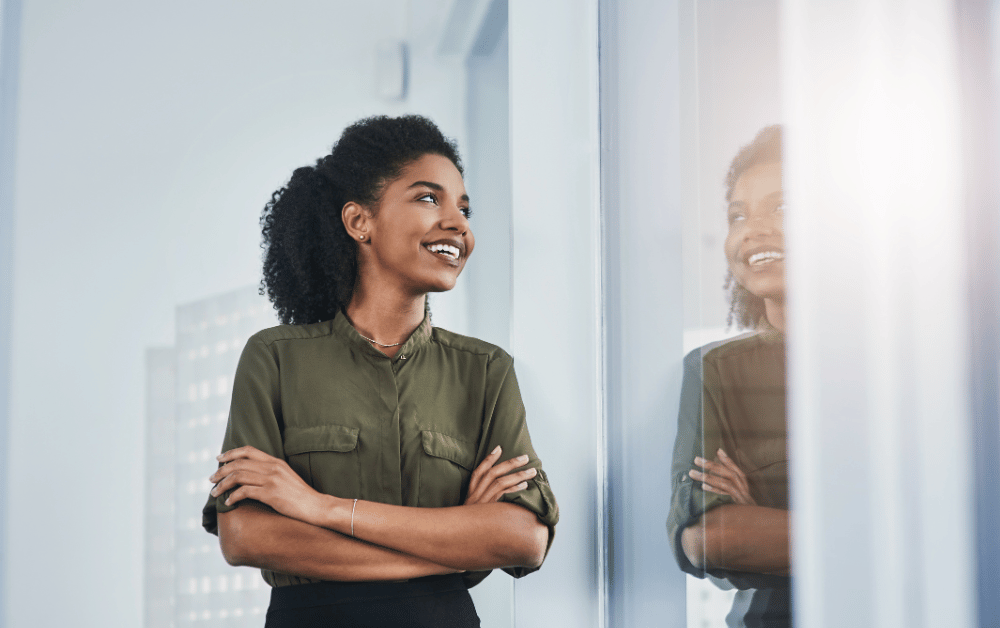 Confident woman smiling while looking out the window, embracing self-worth and overcoming the habit of comparing yourself to others.