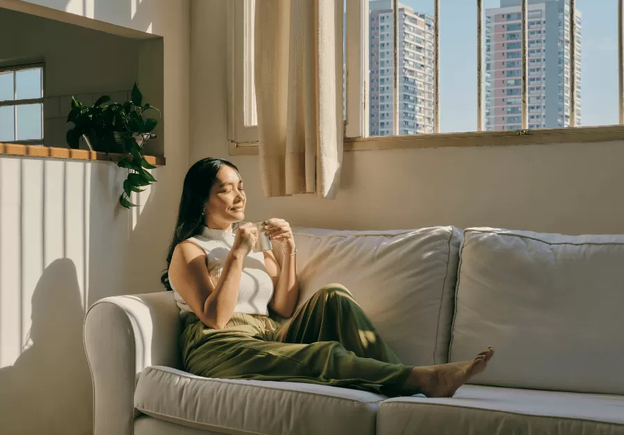 Woman practicing mindful living, sitting quietly on her couch and enjoying a peaceful moment with her coffee.