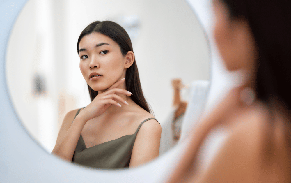 Confident woman in a green top looking at herself in the mirror, symbolizing the benefits of self-awareness, self-acceptance, and mental well-being.