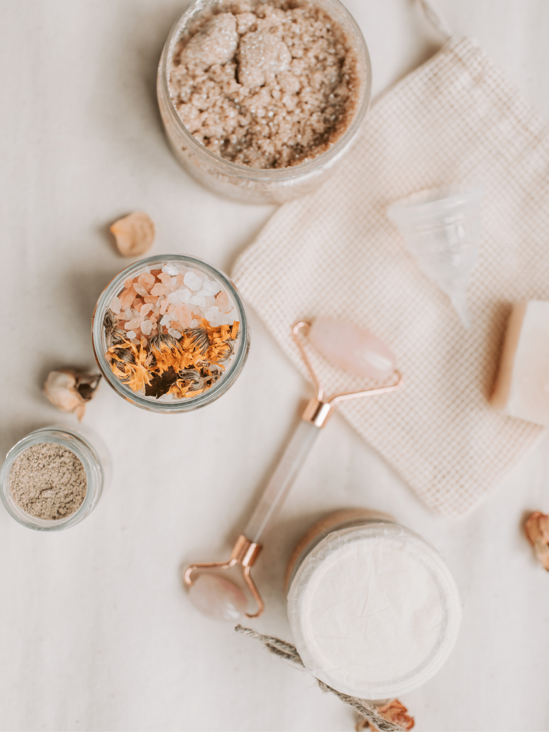 Flat lay of self-care items including bath salts, jade roller, and skincare products, featured on the Goodness of Serenity self-care blog.
