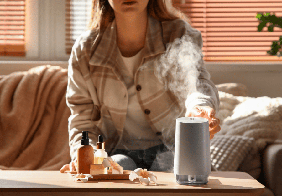 Woman relaxing at home using essential oils with an ultrasonic diffuser releasing mist, preparing aromatic diffuser blends for wellness and relaxation.