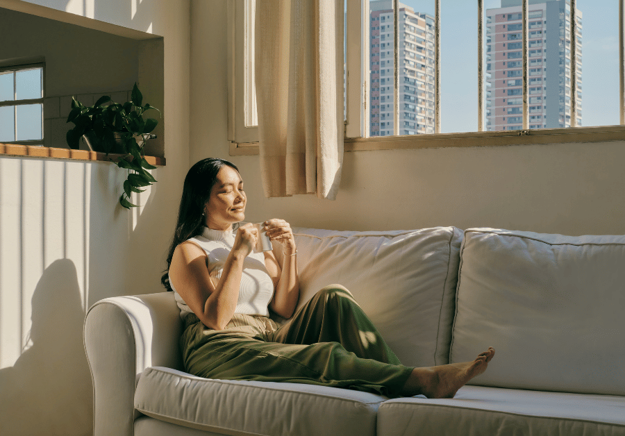 Woman sitting quietly on her couch and enjoying a peaceful moment with her coffee while practicing mindful living tips.