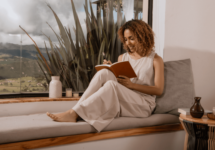 Woman sitting on her couch writing in her journal as part of her morning routine list.