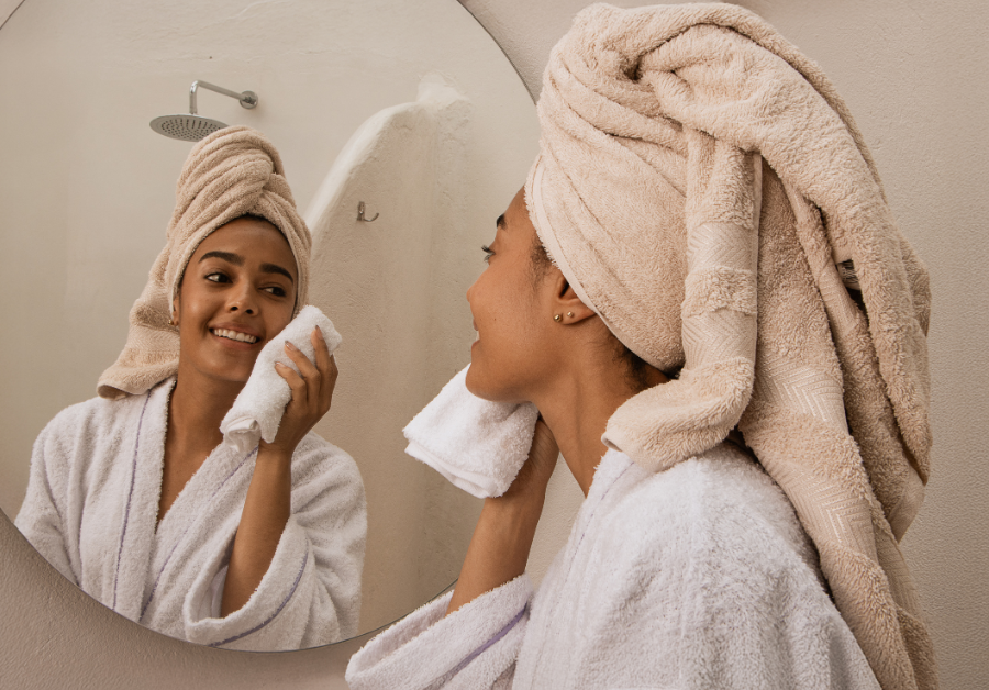 A woman cleansing her face in front of the bathroom mirror as part of her wellness routine.