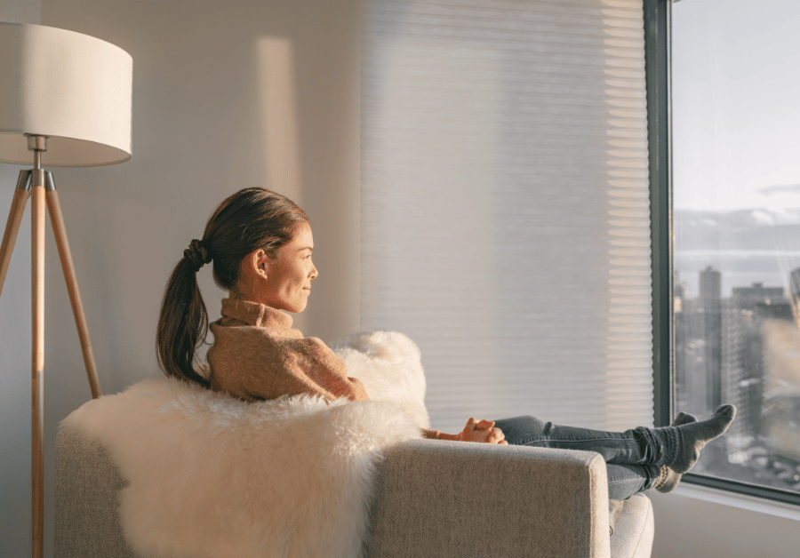 A woman sitting quietly in a calm, softly lit space, reflecting in thought with a relaxed posture, surrounded by subtle calming elements like a warm drink and a journal, representing a ‘self-care day’ focused on rest, mindfulness, and personal reflection.