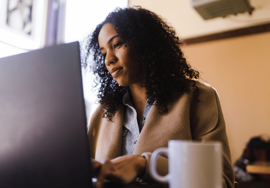 A focused woman working on her laptop at a bright desk, planning and organizing her routine with notes and coffee nearby, representing daily habits for success, productivity, goal setting, and personal growth.