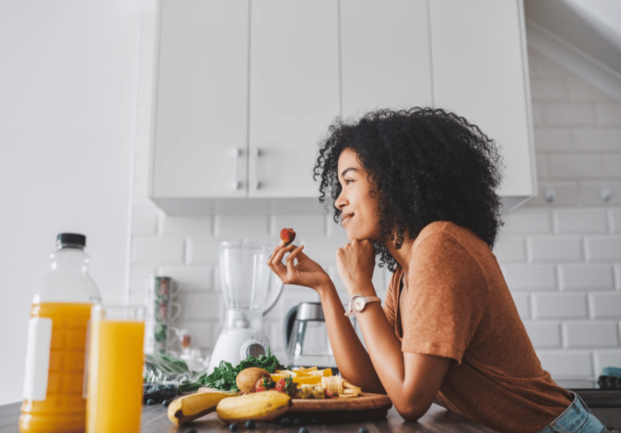 Smiling woman eating healthy food in her kitchen, representing healthy lifestyle tips, healthy eating habits, self care routines, and healthy lifestyle choices in a balanced lifestyle at home.