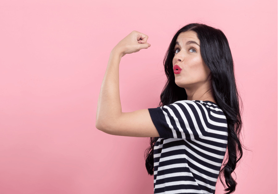 A woman softly flexing her muscle and looking hopeful while learning how to think positive and build confidence.